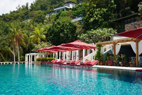 タリンガムビーチにあるConrad Koh Samuiの赤いラウンジチェアとパラソルのあるプール