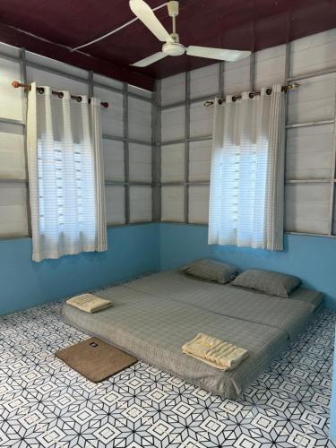 a large bed in a room with two windows at Lazy Mango Home Stay in Phumĭ Poŭthĭ Mâ Srei