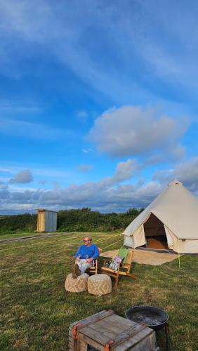 a man sitting on logs in front of a tent at Tiny Treamble in Cubert