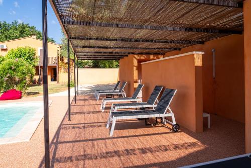 a row of lounge chairs under a pergola next to a pool at Hotel Les Ambres in Roussillon