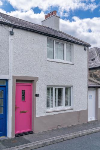 a white house with a pink door on a street at Dolfor in Menai Bridge