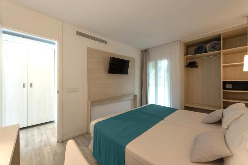 a white bedroom with a bed and a television at Hotel Club Es Talaial in Cala d´Or