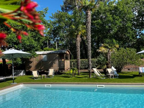a swimming pool with chairs and a tent and palm trees at Villa Herbert Maison d'Hôtes in Andernos-les-Bains