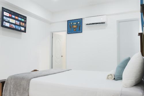 a white bedroom with a bed and a tv on the wall at Hotel Relax Las Terrenas in Las Terrenas