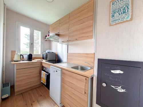 Elle comprend une petite cuisine avec des placards en bois et un évier. dans l'établissement appartement accès direct mer classé 3*, à Cabourg