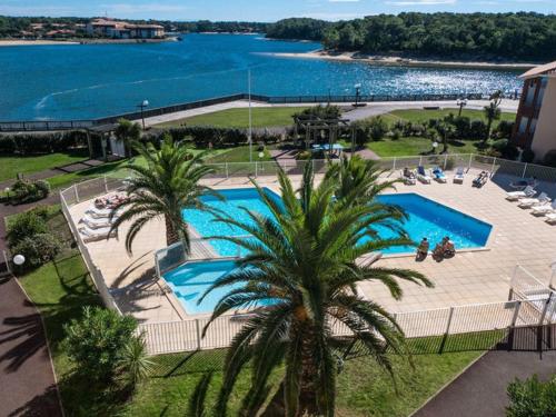 une piscine avec des palmiers à côté d'une masse d'eau dans l'établissement T2 avec piscine, terrasse et parking à Vieux-Boucau - FR-1-379-81, à Vieux-Boucau-les-Bains