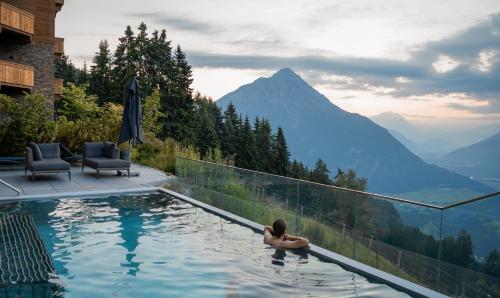 a woman sitting in a swimming pool with a view of mountains at Puitalm Apartments & SPA by Peak Stay in Arzl im Pitztal