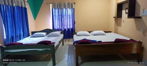 two beds in a room with blue curtains at Hotel Aishwarya New Digha I Near Amrabati Park in Digha