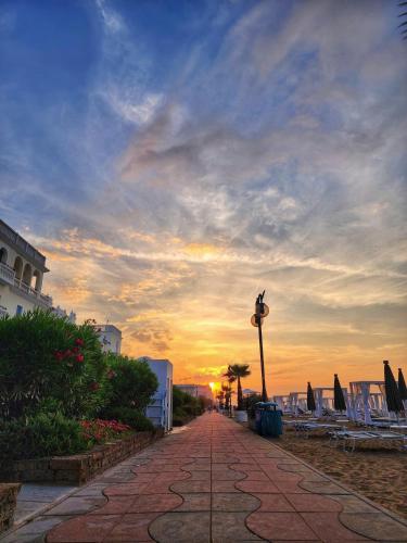 a sunset on a beach with chairs and a sidewalk at Hotel Bellariva in Lido di Jesolo