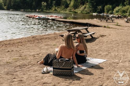 two women sitting on a towel on the beach at Le2089 - Spa et plage - Les chalets dans le nord in Sainte-Lucie-de-Doncaster