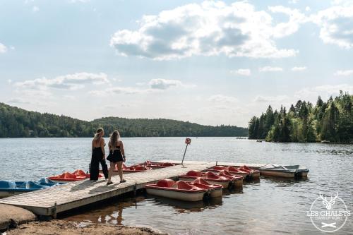 two women standing on a dock with boats on a lake at Le2085 - Spa et Plage - Les chalets dans le nord in Sainte-Lucie-de-Doncaster