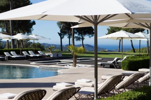 a pool with chairs and umbrellas next to a pool at L'Hôtel & Spa du Castellet in Le Castellet
