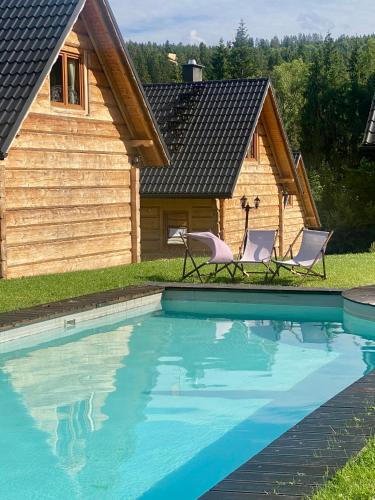 a house with two chairs next to a swimming pool at domki z dostępem do SPA i restauracji in Łapsze Niżne
