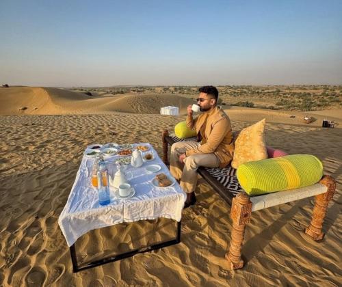 斋沙默尔Hotel Hostel Stay Jaisalmer的一名男子坐在沙漠中打电话