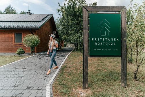 a woman walking past a sign in front of a house at Przystanek Roztocze in Susiec