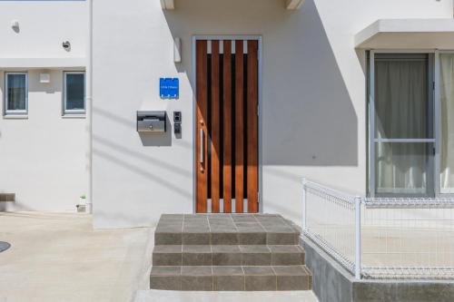 a wooden door on a white building with stairs at 沖縄うるま市 最大9名OK BBQ 徒歩1分で天然ビーチ 広々3部屋の快適ステイ Villa Ohana in Uruma