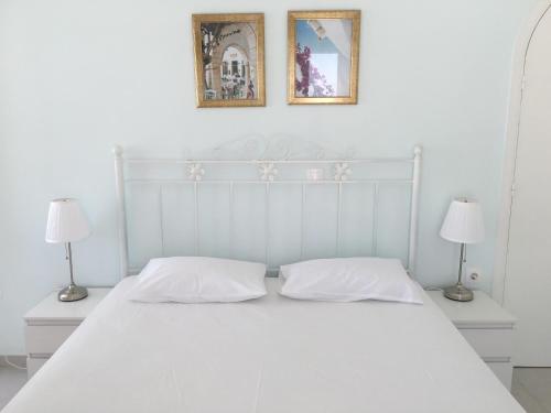 a white bed with two lamps and two pictures on the wall at Nikoleta Rooms in Tinos Town