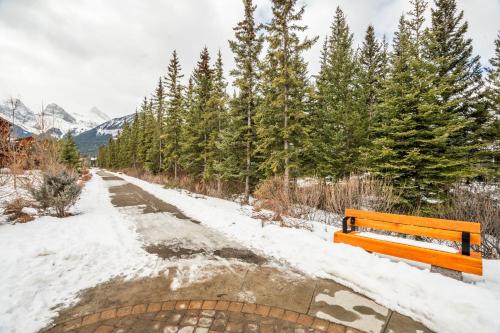 a wooden bench sitting on a snow covered path at Spring Creek Penthouse by Canadian Rockies Vacation Rentals in Canmore