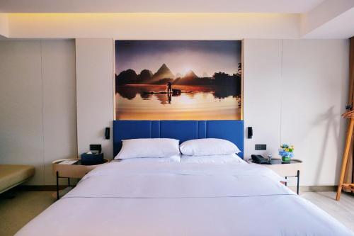 a bedroom with a large bed with a painting on the wall at Magnotel Guilin Elephant Trunk Hill in Guilin