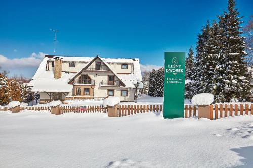 a house covered in snow with a fence and a sign at Leśny Dworek - Pokoje & Apartamenty in Białka Tatrzanska