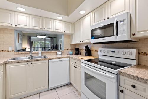 a kitchen with white cabinets and a sink and a microwave at Siren’s Song, Minutes to IMG & Anna Maria Island in Bradenton