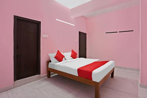 SurūrnagarにあるHotel O Sruan Inn Kamineni Bus Stopのピンクの壁のベッドルーム1室、赤い枕付きのベッド1台が備わります。