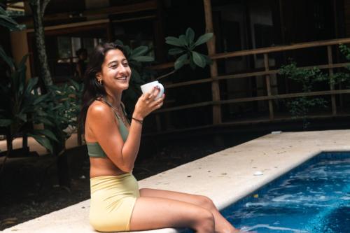 a woman in a bikini sitting next to a swimming pool at Rusteak Living Retreat in natural and peaceful setting in Canafistula in Cañafístula