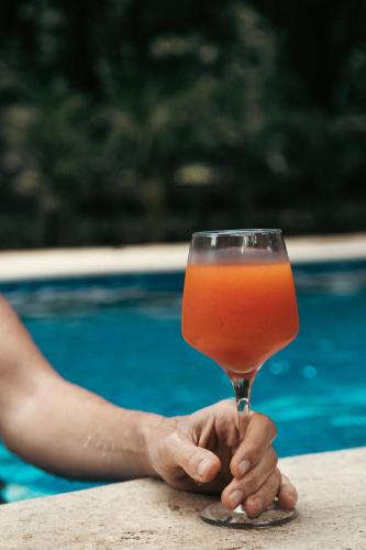 a person holding a glass of orange drink next to a swimming pool at Rusteak Living Retreat in natural and peaceful setting in Canafistula in Cañafístula