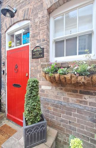 una puerta roja en una casa de ladrillo con plantas en Ironbridge View Townhouse WINNER 2025 UK MOST PICTURESQUE SELF-CATERING HOLIDAY HOME & WINNER SELF-CATERING ACCOMMODATION OF THE YEAR 2025, en Ironbridge