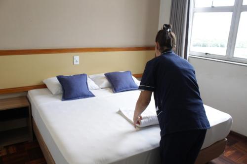 a woman standing next to a large bed at Pouso Alegre Hotel INN - Próximo a Unimed e Rodoviária in Pouso Alegre