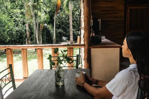 a woman sitting at a table with a cup of coffee at Rusteak Living Retreat in natural and peaceful setting in Canafistula in Cañafístula