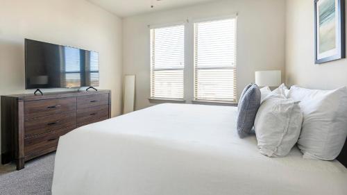 a white bedroom with a large bed and a television at Landing at The Flats at Shadowglen - Manor in Manor