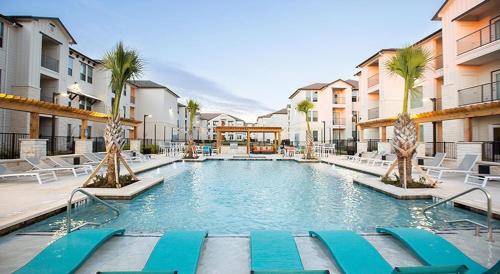 a swimming pool with chairs and palm trees and buildings at Landing at The Flats at Shadowglen - Manor in Manor