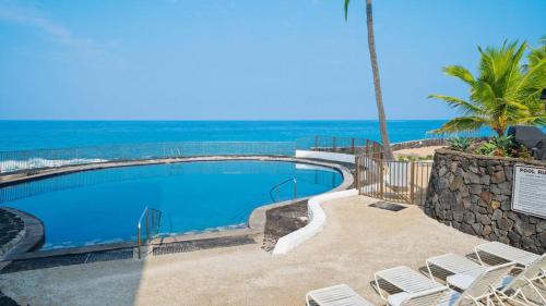 a swimming pool with chairs and the ocean in the background at Casa De Emdeko Condo with Pool AC & Ocean Views in Kailua-Kona