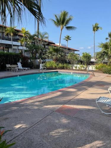 a swimming pool in front of a building with palm trees at Casa De Emdeko Condo with Pool AC & Ocean Views in Kailua-Kona