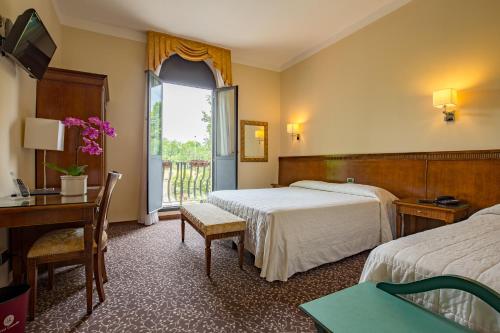 a hotel room with two beds and a desk and a window at Hotel Castello in Modena