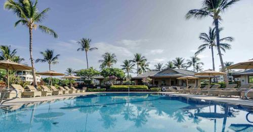 a swimming pool at a resort with chairs and palm trees at Kolea 11D - Walk to the Beach in Waikoloa