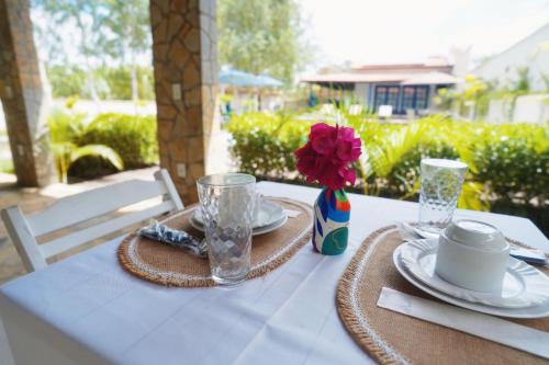 a table with plates and a vase with a flower on it at Pousada Vila Pequi in Barreirinhas