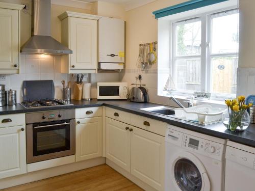 a kitchen with white cabinets and a sink and a dishwasher at Teal Cottage in Embleton