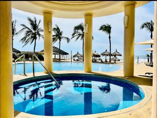 a pool at a resort with palm trees and a beach at FRENTE AL MAR A PIE DE PLAYA ALBERCA y JACUZZI 7 in Mazatlán
