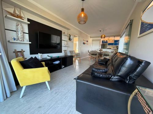 a living room with a black leather couch and a yellow chair at Apartamento em Ubatuba com vista para o mar in Ubatuba