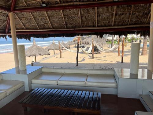 a view of a beach with a couch and umbrellas at FRENTE AL MAR A PIE DE PLAYA ALBERCA y JACUZZI 7 in Mazatlán