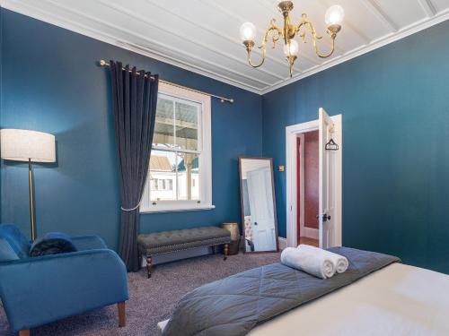 ein blaues Schlafzimmer mit einem Bett und einem Stuhl in der Unterkunft Creed Cottage - Whitianga Heritage Retreat in Whitianga
