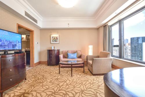 a living room with a tv and a couch and chairs at Furama Hotel Dalian in Dalian
