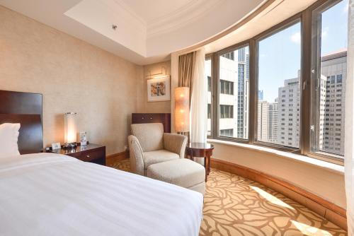 a hotel room with a bed and a chair and windows at Furama Hotel Dalian in Dalian