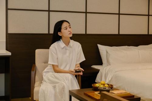 a woman sitting in a chair next to a bed at Aank Ryokan Hotel Suwon in Suwon