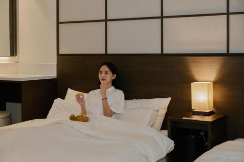 a woman sitting in bed with a bowl of fruit at Aank Ryokan Hotel Suwon in Suwon
