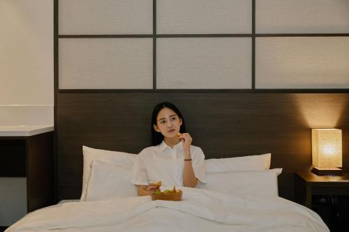 a woman sitting on a bed with a plate of food at Aank Ryokan Hotel Suwon in Suwon