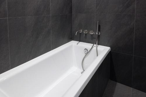 a white bath tub in a bathroom with black tiles at Aank Ryokan Hotel Suwon in Suwon