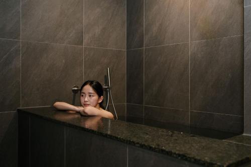 a woman is standing in a bathroom sink at Aank Ryokan Hotel Suwon in Suwon